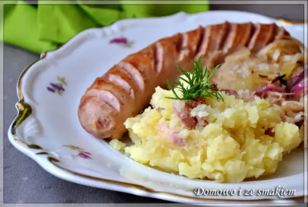 Biała kiełbasa z ziemniakami i kapustą kiszoną, udekorowana koperkiem.