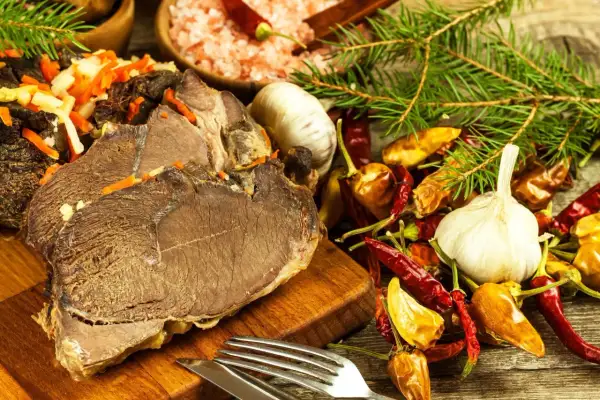 Gotujesz dziczyznę? Na stole pieczone mięso, czosnek, papryczki chili i przyprawy. Idealne składniki, by dowiedzieć się, jak przyrządzić dziczyznę.