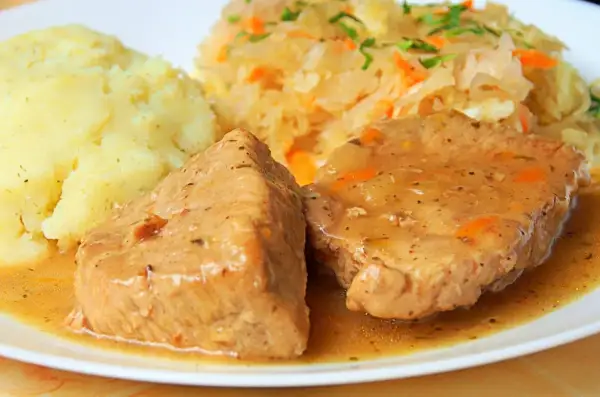 Soczysta szynka wieprzowa w sosie, podana z puree ziemniaczanym i surówką z kiszonej kapusty. Idealny pomysł, jak zrobić szynkę wieprzową na obiad.