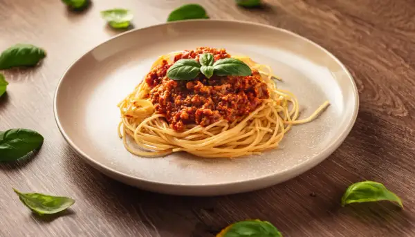 Talerz spaghetti z sosem bolońskim i listkami bazylii na drewnianym tle.