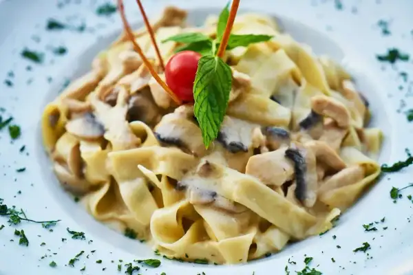 Tagliatelle z kurczakiem i grzybami w sosie śmietanowym, udekorowane pomidorkiem i miętą.