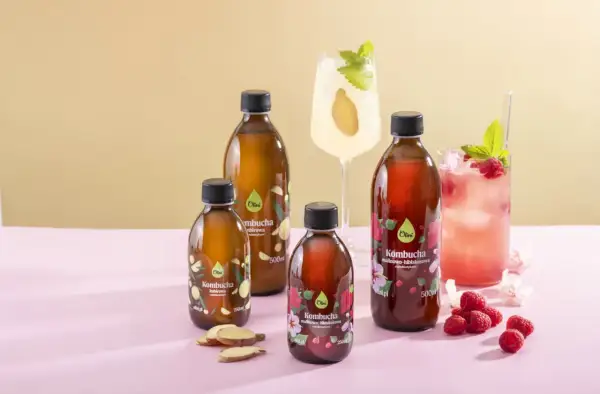 Butelki z kombuchą, drinki, maliny i imbir na różowym tle.