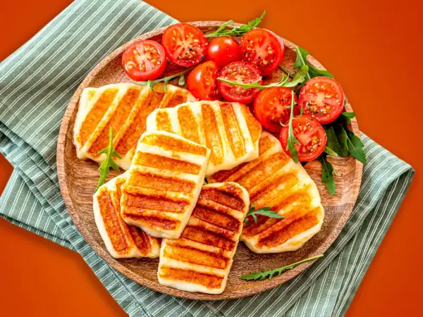 Grillowany ser halloumi z pomidorkami koktajlowymi na drewnianej desce.