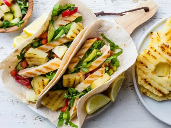 Tacos z grillowanym kurczakiem, ananasem i warzywami, podane z cytryną.