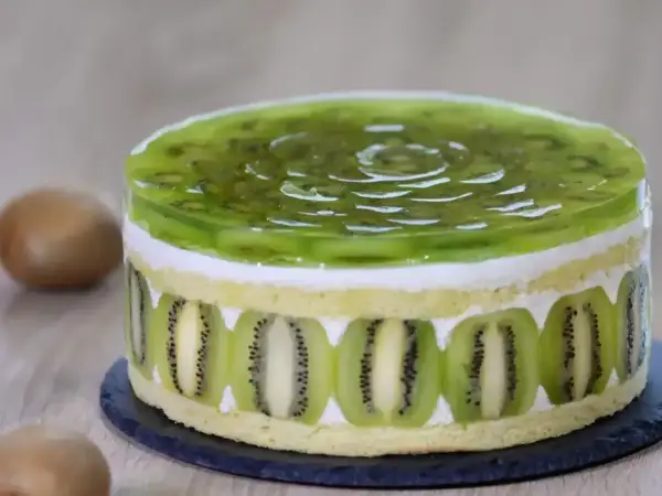 Tort z galaretką kiwi i plasterkami kiwi na bokach.