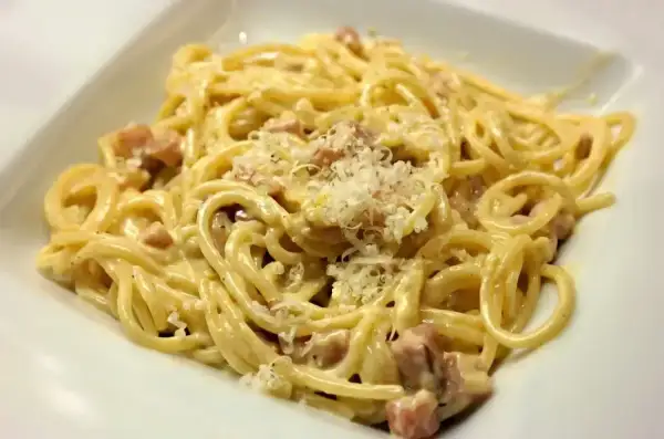 Porcja spaghetti carbonara z kawałkami boczku i startym parmezanem.