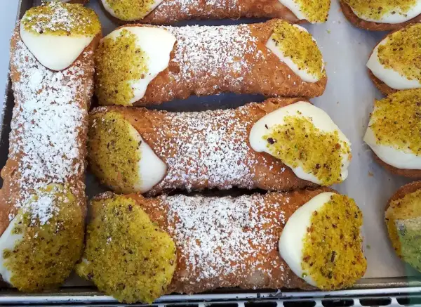 Sycylijskie cannoli z kremem i pistacjami, posypane cukrem pudrem.
