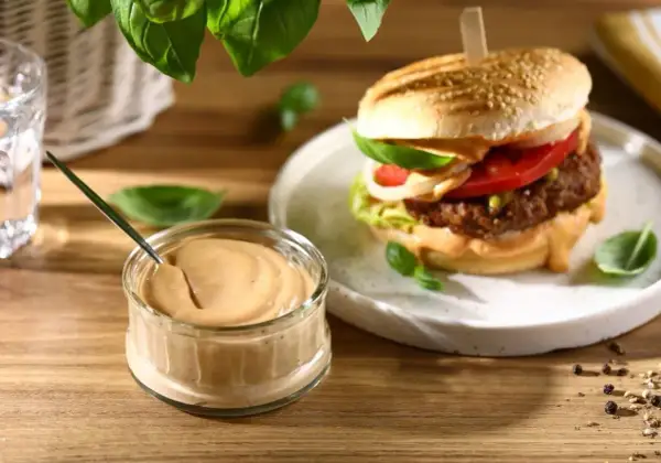 Domowy sos do burgerów w słoiczku obok gotowego burgera na talerzu.