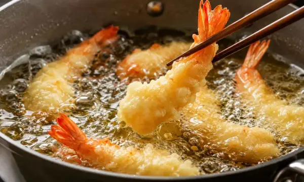 Krewetki w cieście tempura smażące się na złoty kolor w gorącym oleju.