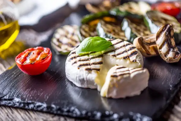 Grillowany ser Camembert z pomidorkiem i warzywami na czarnym kamieniu.