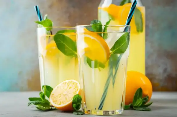 Dwa szklanki orzeźwiającej lemoniady z cytryną i miętą, obok cytryny i dzbanka z napojem.