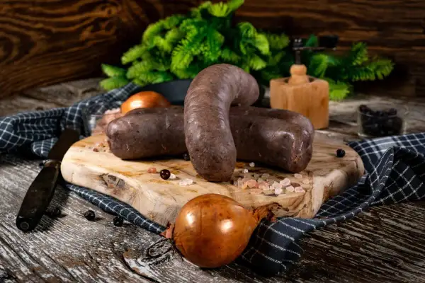 Kaszanka na desce z cebulą i przyprawami. Idealne składniki, by dowiedzieć się, co dodać do kaszanki, by była pyszna.