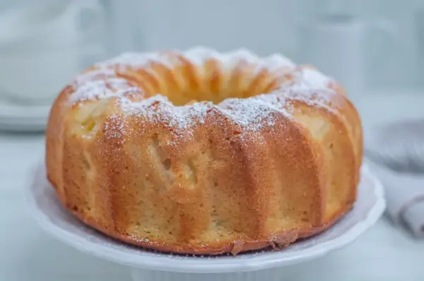 Puszysta babka cytrynowa posypana cukrem pudrem na białej paterze.