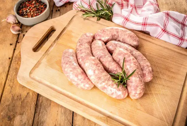 Surowe kiełbaski na desce, obok przyprawy i czosnku. Zastanawiasz się, jak długo parzyć kiełbasę, by była idealna?