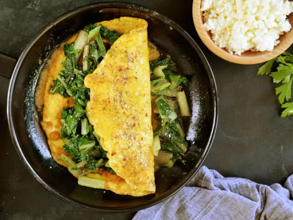 Omlet z serka wiejskiego z zielonymi warzywami na patelni.