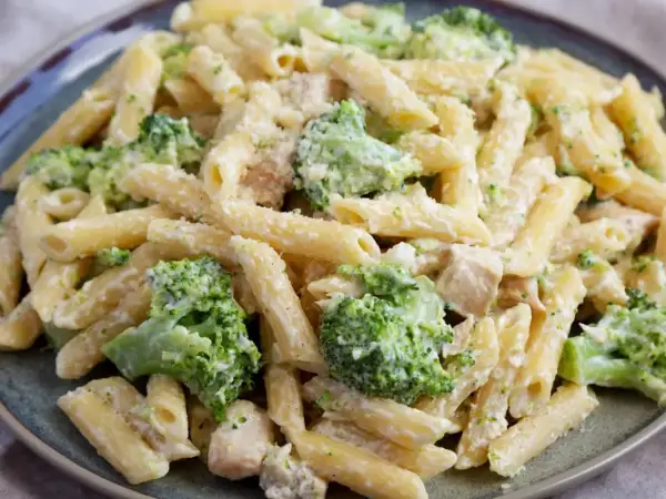 Makaron penne z brokułami i kurczakiem w kremowym sosie na talerzu.