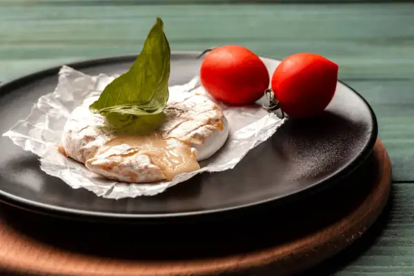 Grillowany ser camembert z pomidorkami koktajlowymi i bazylią na talerzu.