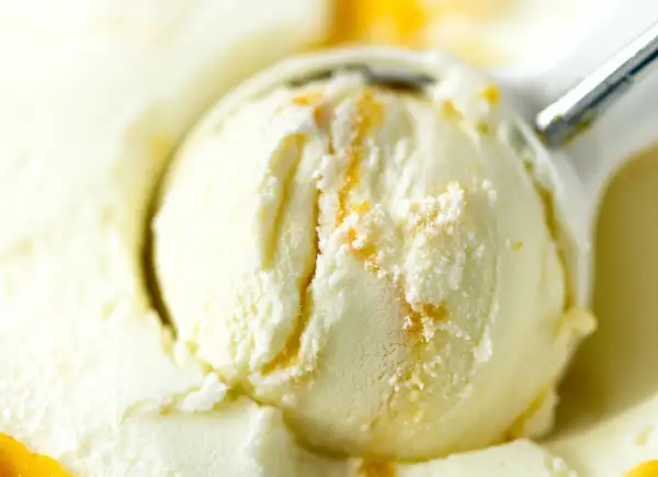 Łyżka do lodów nakłada kremowe lody waniliowe z pomarańczowymi smugami.
