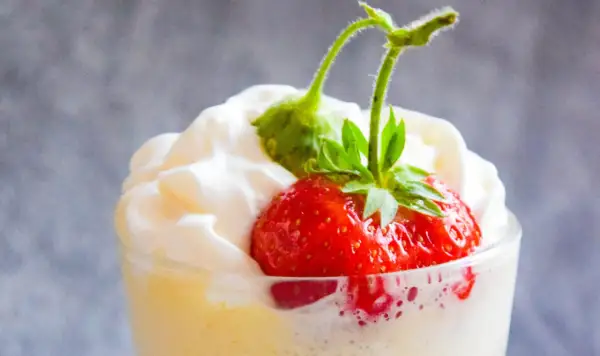 Deser zabaglione z truskawką i bitą śmietaną w szklance.