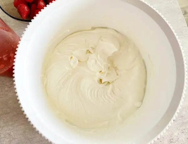 Krem z mascarpone w białej misie, obok miseczka z truskawkami.
