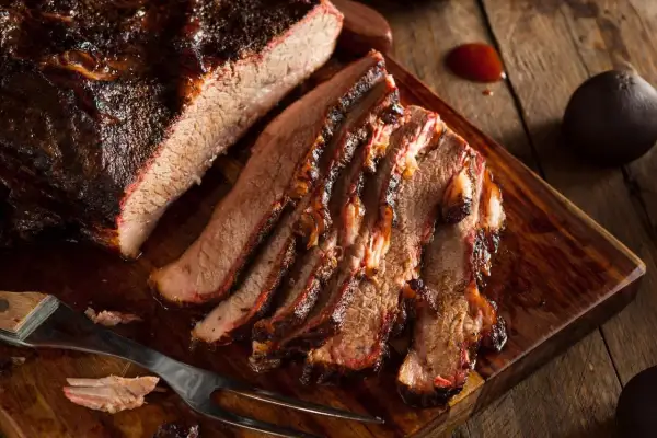 Pokrojona wołowina brisket z ciemną skórką, ułożona na drewnianej desce.