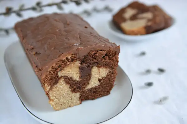 Wilgotna babka marmurkowa z czekoladową polewą na białym talerzyku.