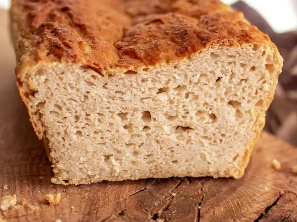 Przekrojony bochenek chleba bezglutenowego na drewnianej desce, z widocznym puszystym wnętrzem.
