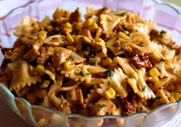 Sałatka z makaronem farfalle, kurczakiem, kukurydzą i suszonymi pomidorami w szklanej misie.