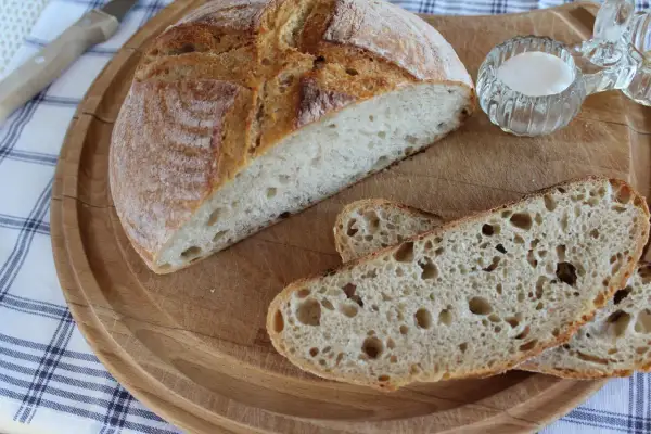 Chleb pszenno-żytni na zakwasie, przekrojony bochenek i kromki na desce.