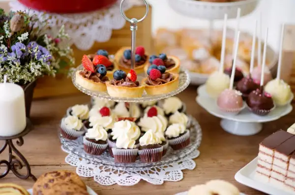 Stół z babeczkami, tartaletkami z owocami, cake pops i ciastem.