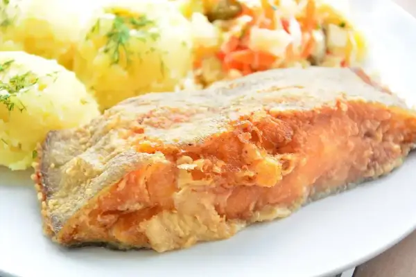 Smażony filet z ryby z ziemniakami i surówką na talerzu.
