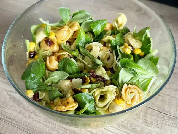 Sałatka z tortellini, kukurydzą, suszonymi pomidorami i zieloną sałatą w szklanej misce.