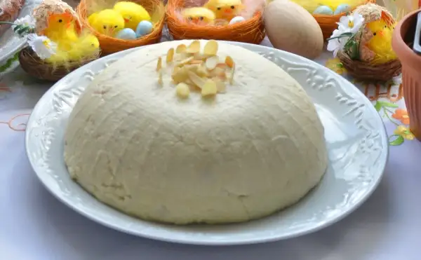 Pascha na białym talerzu, ozdobiona płatkami migdałów, w tle wielkanocne kurczaczki.