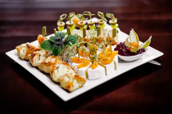 Talerz z przekąskami finger food: ciastka francuskie, sery, pomidorki koktajlowe, oliwki i dżem.