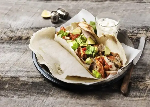 Tortilla z kurczakiem, awokado i sosem na drewnianym stole.