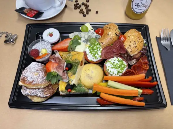 Taca ze śniadaniem kontynentalnym: naleśniki, omlet, sery, wędliny, owoce, warzywa i napój.