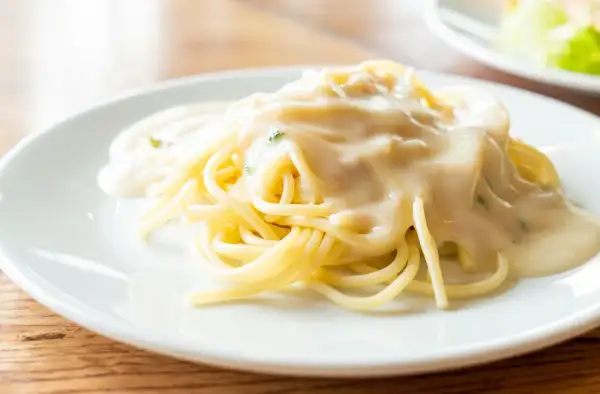 Kremowy sos serowy na makaronie spaghetti na białym talerzu.