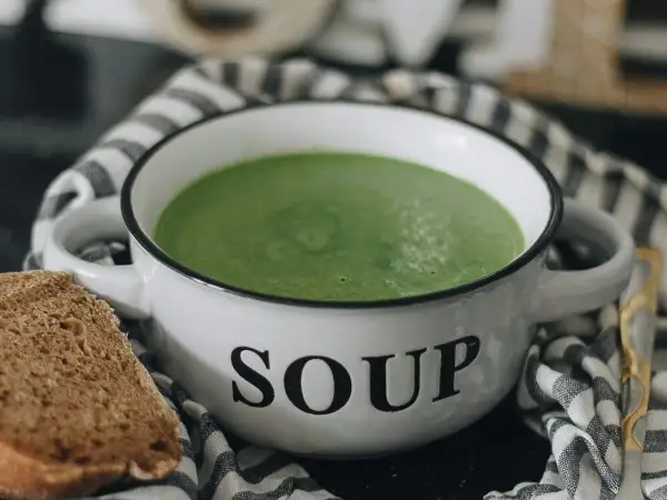 Zielony kremowy zupa w misce z napisem "SOUP". Idealna do mrożenia zup, by cieszyć się smakiem przez cały rok. Obok kromka chleba.