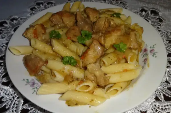 Penne z soczystym makaronem z mięsem wieprzowym w sosie, udekorowane natką pietruszki.