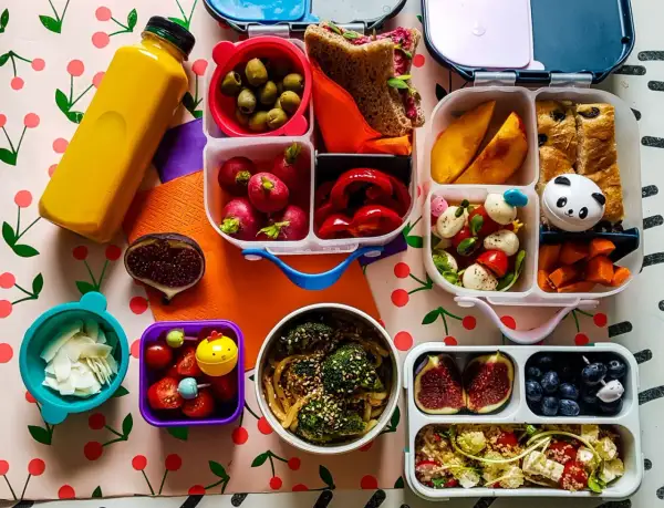 Kolorowy lunchbox z owocami, warzywami, kanapką i napojem.