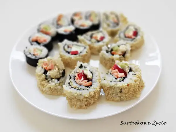 Talerz z rolkami sushi uramaki, niektóre obtoczone w sezamie, z widocznym łososiem i warzywami.