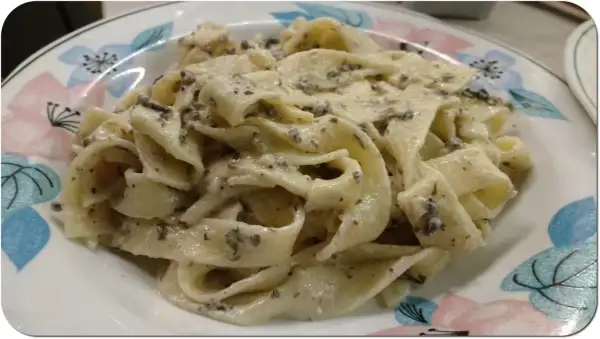 Pappardelle z kremowym sosem, w którym wyczuwalne są kawałki trufli. Makaron z pastą truflową i śmietaną wygląda apetycznie.